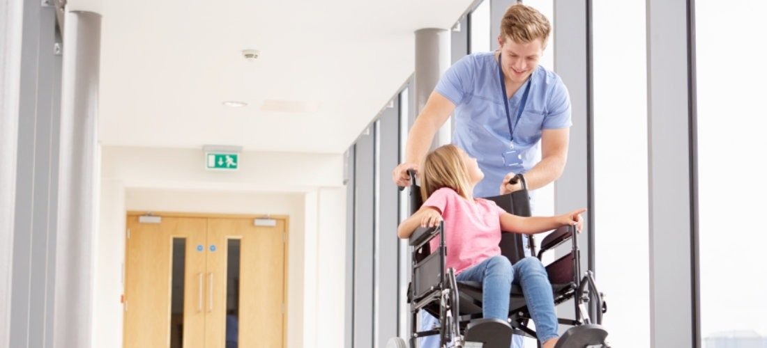 Foto Pfleger betreut Kind im Rollstuhl beide sind fröhlich